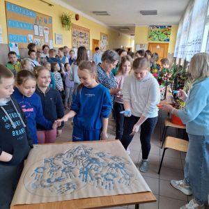 Wesoła grupa dzieci odbija na papierze swoje dłonie pomalowane na niebiesko