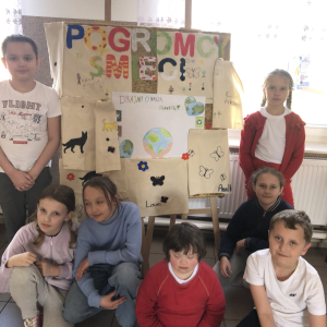 Dzieci z klasy III siedzą koło plakatu oraz ozdobionych worków ekologicznych