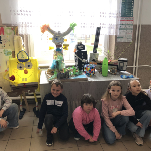 Dzieci z klasy III siedzą obok wystawy prac „Drugie życie śmieci „