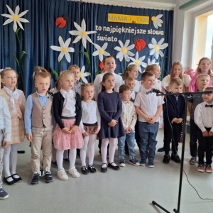 Grupa dzieci z klas 0-III stoi i śpiewa na tle dekoracji