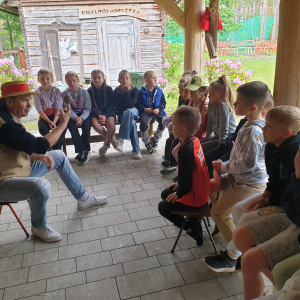 Grupa dzieci siedzi i słucha opowieści gospodarza zagrody 