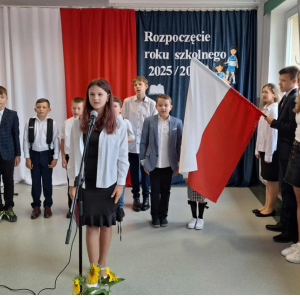 Uczniowie kl. 2 i 5 stoją na baczność przed gazetka szkolną rozpoczynającą nowy rok szkolny i śpiewają hymn narodowy