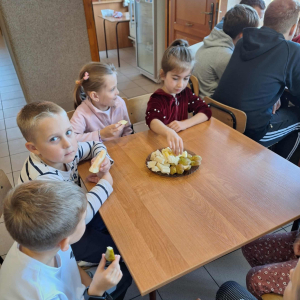 Uczniowie jedzą przy stolikach owoce.