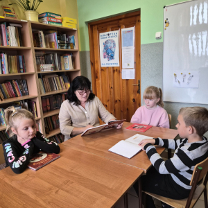Uczniowie słuchają fragmentu książki czytanej przez panią bibliotekarkę.