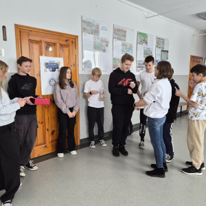 Najstarsi uczniowie stoją na korytarzu, losują karteczki z przykładami mnożenia i udzielają odpowiedzi