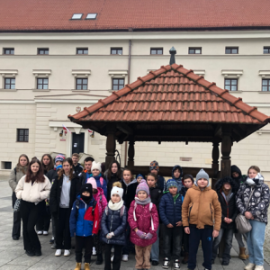 Uczniowie stoją przed studnią na tle muzeum.