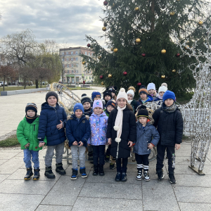  Dzieci stoją przed choinką i saniami na placu SOK, ciesząc się świąteczną atmosferą.