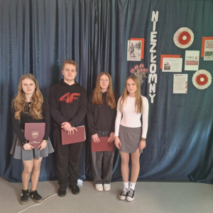 Uczniowie klasy VIII stoją na tle dekoracji przygotowanej z okazji Narodowego Dnia Pamięci „Żołnierzy Wyklętych"