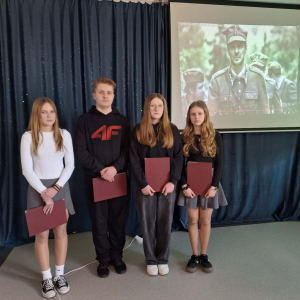 Uczniowie stoją na tle slajdu przedstawiającego żołnierzy 